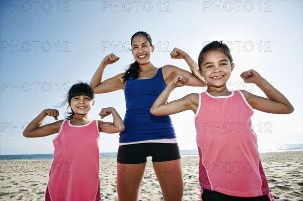 Mother and daughters flexing muscles at beach