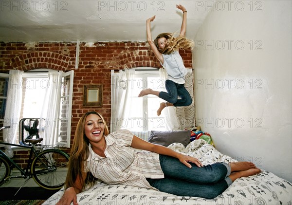 Native American mother and daughter jumping on bed