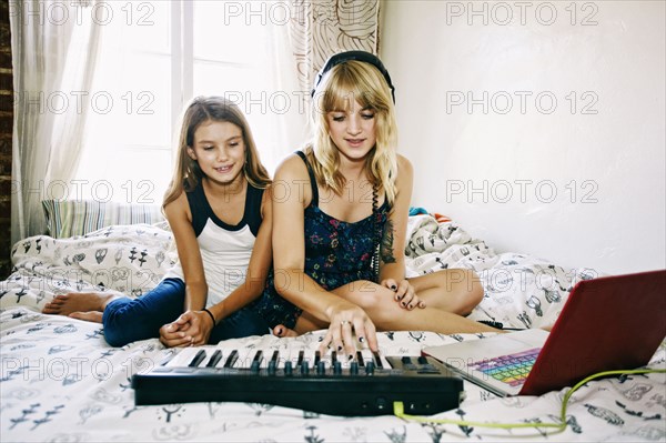 Sisters playing keyboard on bed