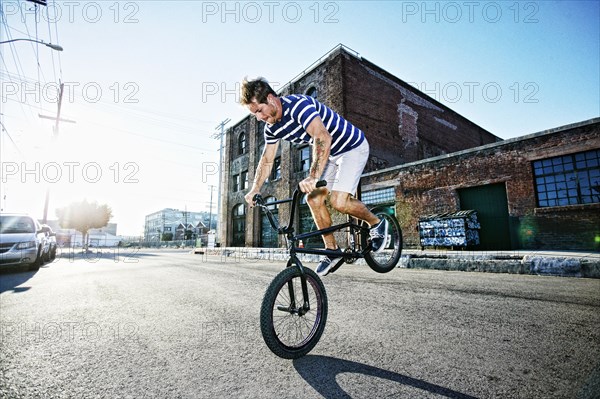 Caucasian man riding BMX bike on street