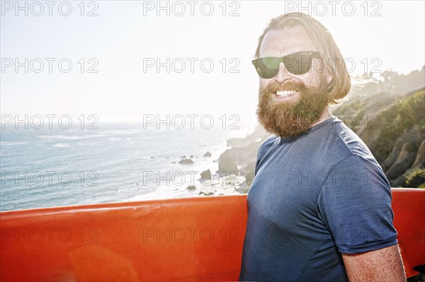 Caucasian man holding surfboard on coastal cliff