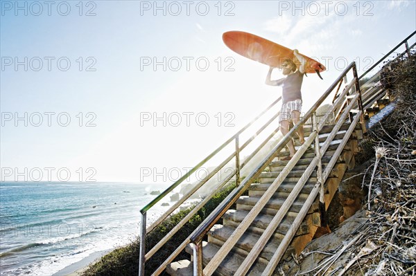 Caucasian man carrying surfboard on stairs at beach