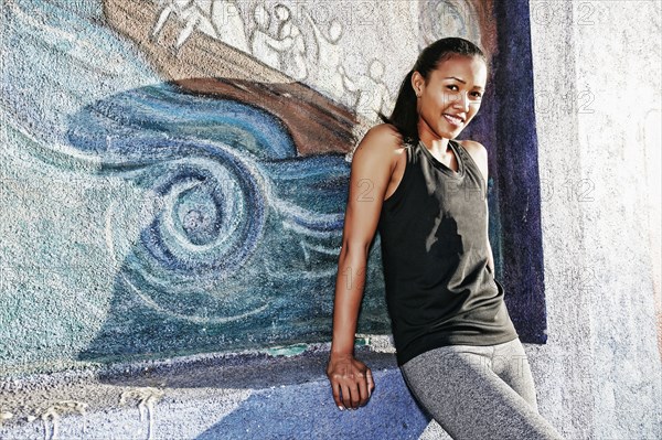 Mixed race athlete sitting on mural wall