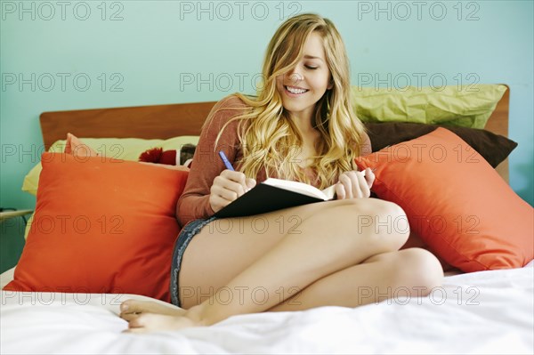 Caucasian woman writing in diary on bed