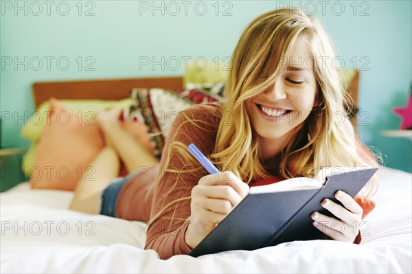 Caucasian woman writing in diary on bed