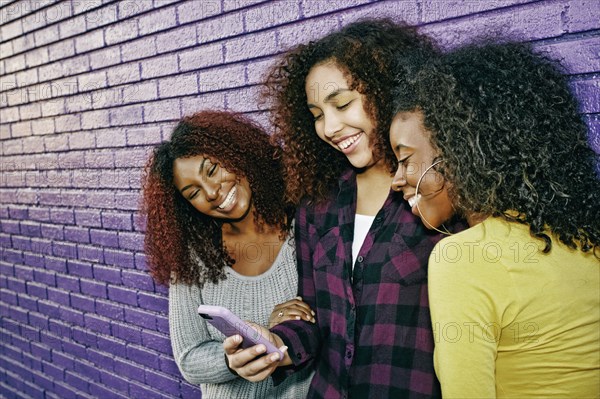 Women using cell phone outdoors at purple wall