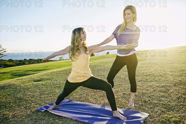 Caucasian woman practicing yoga with trainer in field