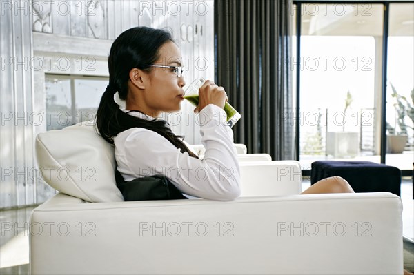 Chinese businesswoman drinking green smoothie on sofa