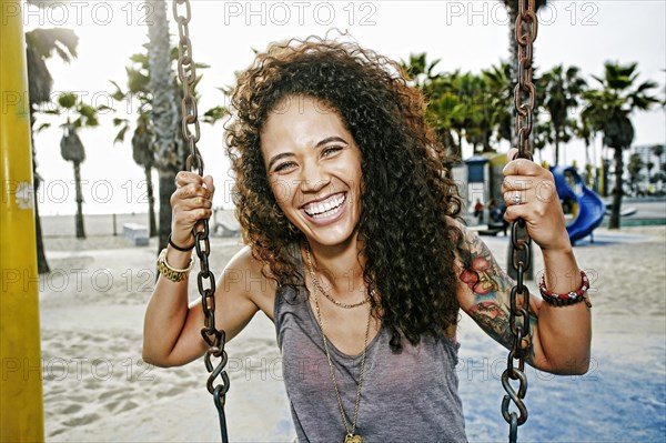 Mixed race woman sitting on swing at beach