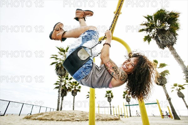 Mixed race woman playing on swing at beach