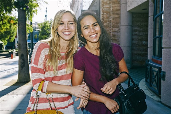 Women walking arm-in-arm on sidewalk