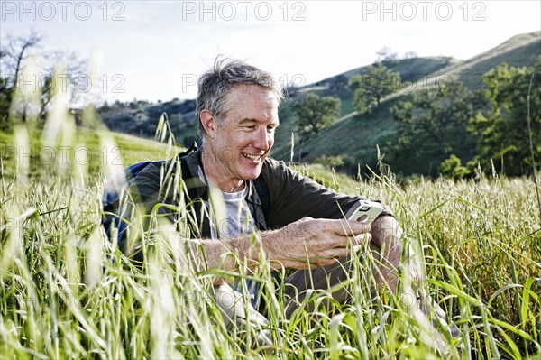 Caucasian hiker sitting in tall grass using cell phone