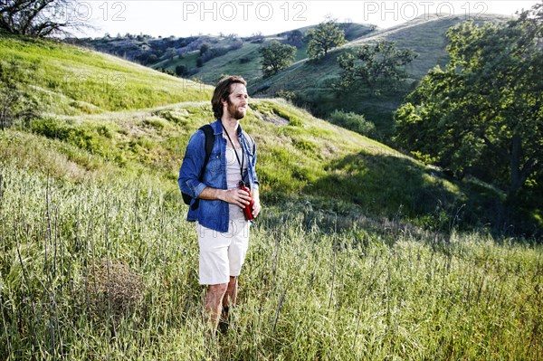 Caucasian hiker standing in grass on mountain holding water bottle