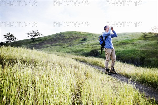 Caucasian man using binoculars on dirt path