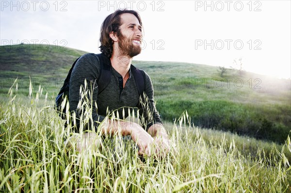 Caucasian hiker crouching in grass on mountain