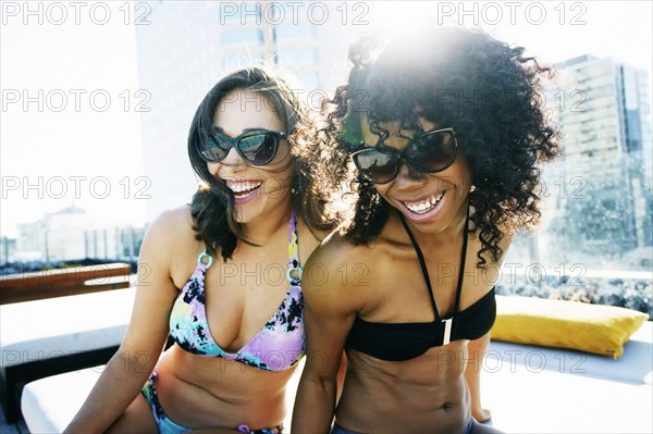 Smiling women wearing bikinis at urban poolside