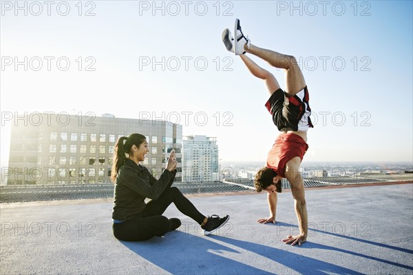 Woman photographing man doing handstand on urban rooftop