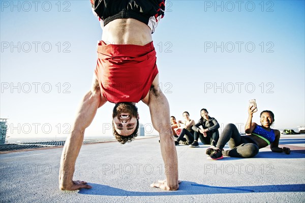 Woman photographing man doing handstand on urban rooftop