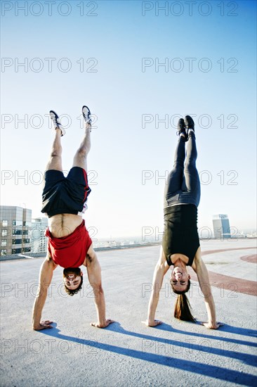 Caucasian couple doing handstands on urban rooftop
