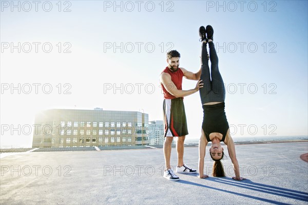 Caucasian man helping woman do handstand on urban rooftop