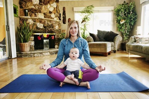 Mother meditating on exercise mat with baby in lap