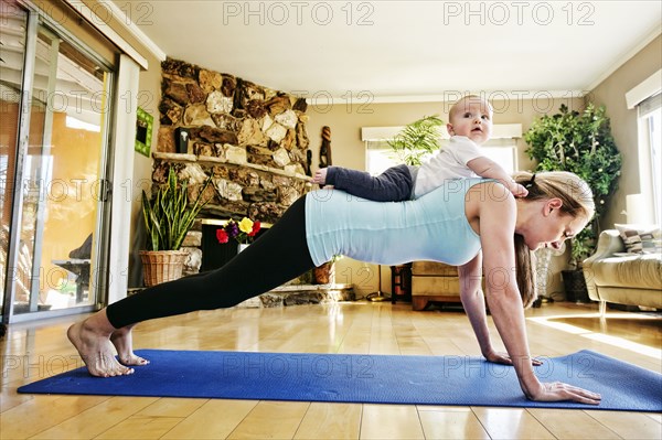Mother working out on exercise mat with baby on back