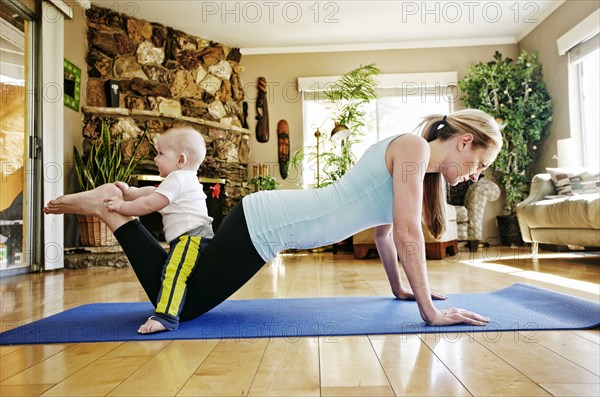 Mother working out on exercise mat with baby on legs