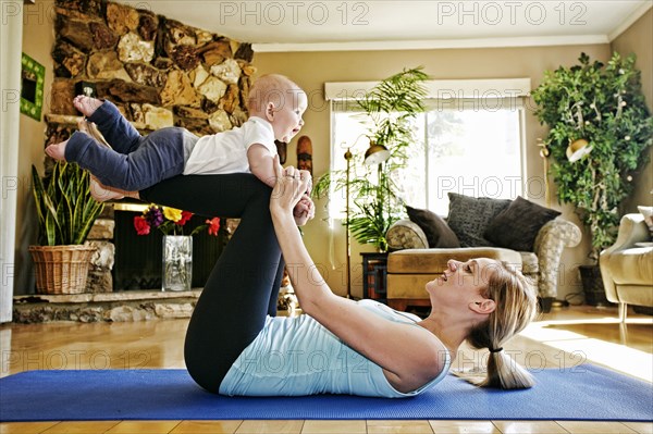 Mother working out on exercise mat balancing baby on legs