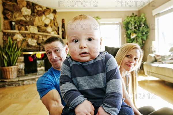 Mother and father posing behind baby on livingroom floor