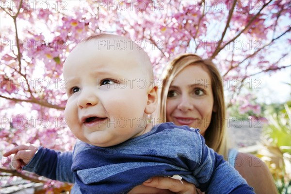 Mother holding baby son under spring tree