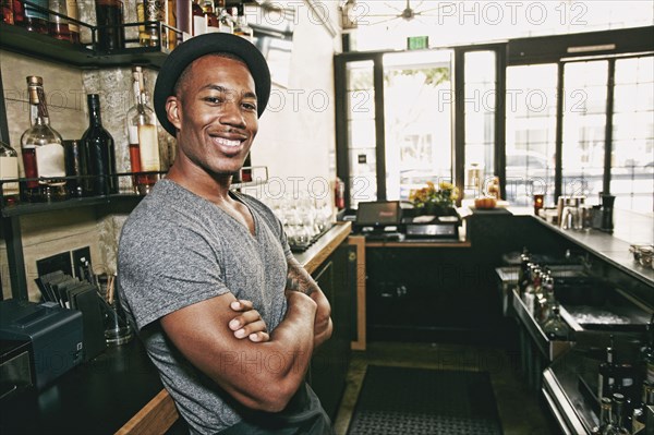 Smiling Black bartender relaxing behind bar