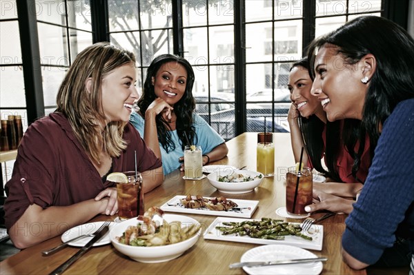 Smiling friends enjoying food and cocktails at table in bar