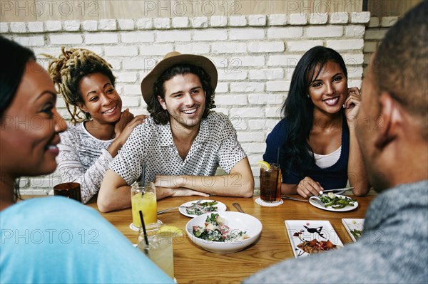 Smiling friends enjoying food and cocktails at table in bar