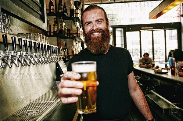Smiling Caucasian bartender serving beer at bar