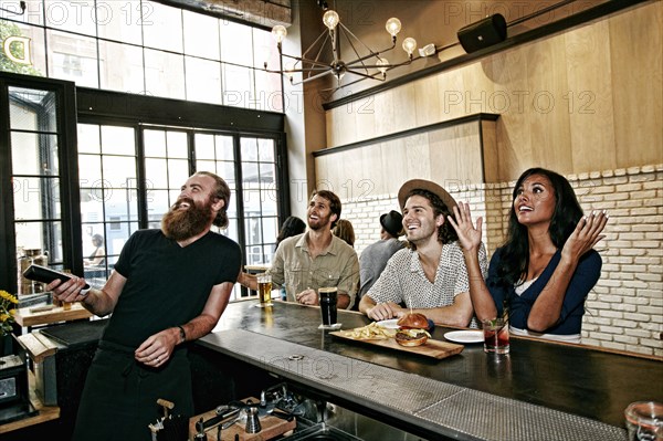 Smiling bartender and customers watching television in bar