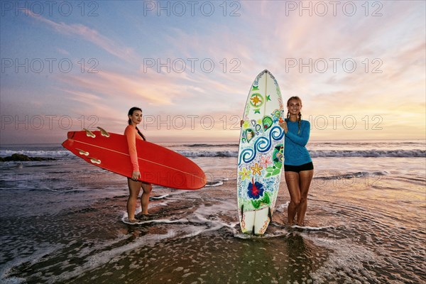 Women standing in ocean waves holding surfboards at beach