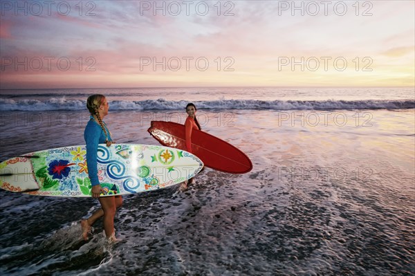 Women carrying surfboards in ocean waves at beach