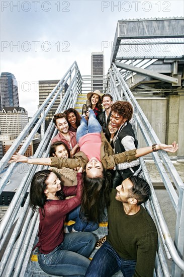 Stylish friends holding woman upside-down on urban metal staircase