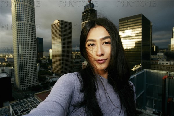 Hispanic woman posing for cell phone selfie on urban rooftop