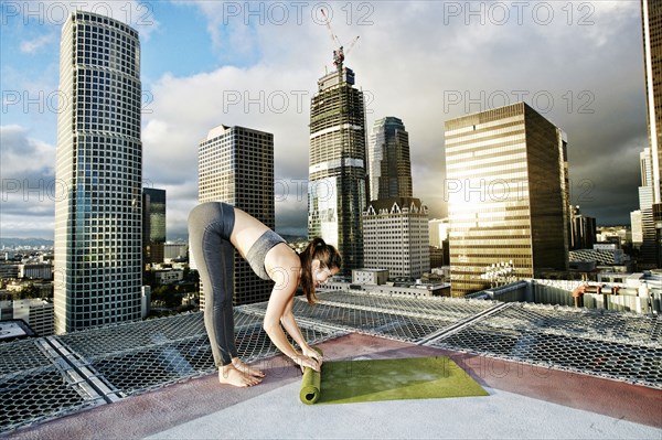 Caucasian woman rolling exercise mat on urban rooftop after yoga