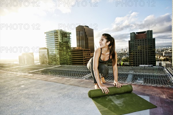 Caucasian woman rolling exercise mat on urban rooftop after yoga