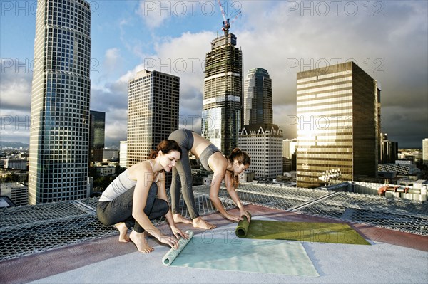 Caucasian women rolling exercise mats on urban rooftop after yoga