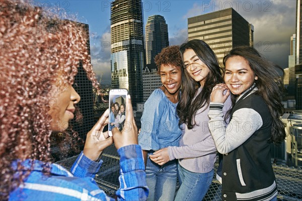 Stylish woman photographing friends on urban rooftop with cell phone