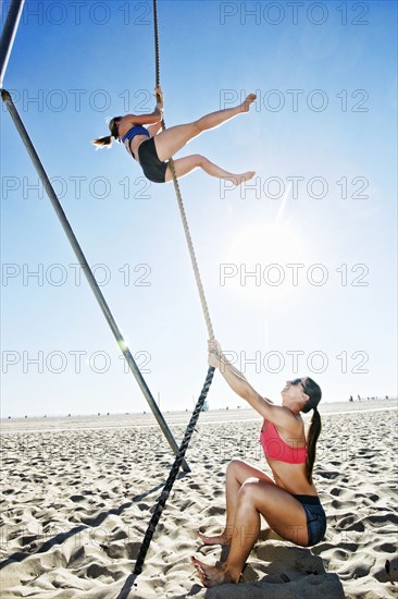 Woman spotting friend climbing rope on beach
