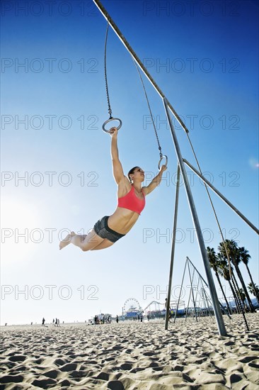 Caucasian woman using gymnastic rings at beach