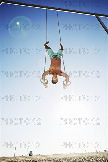 Caucasian man using gymnastic rings at beach