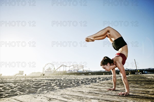 Caucasian woman balancing in handstand on beach boardwalk