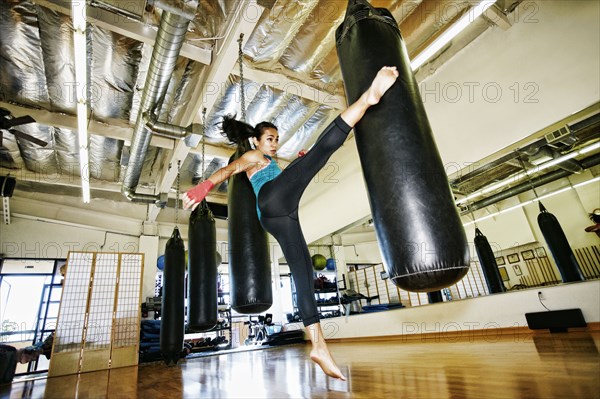 Asian woman kicking heavy bag in gymnasium