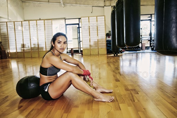 Asian woman leaning on heavy ball in gymnasium