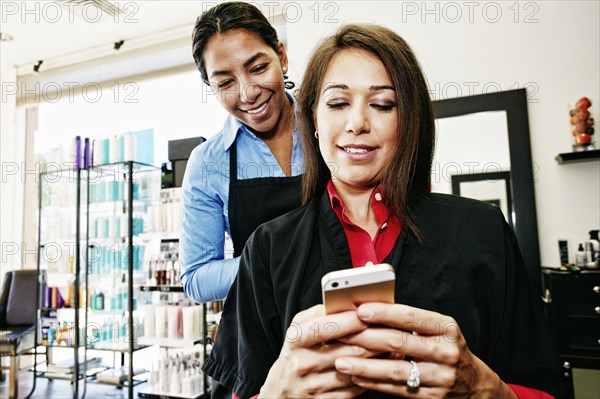 Hairdresser watching customer texting on cell phone in hair salon